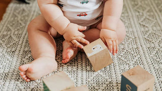 Baby greift nach Holzwürfel — fördert Feinmotorik und Koordination